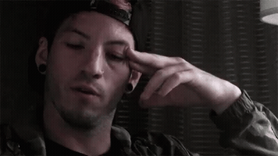 A Man Wearing A Hat And A Jacket Is Holding His Hand To His Forehead . GIF
