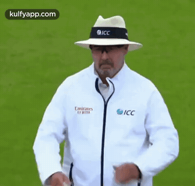 A Man Wearing A Hat And A Jacket That Says Emirates Fly Better Is Standing On A Field . GIF