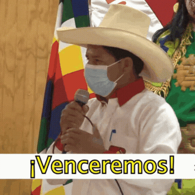 A Man Wearing A Hat And A Mask Holds A Microphone In Front Of A Banner That Says Venceremos GIF