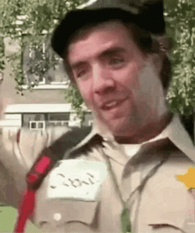 A Man Wearing A Hat And A Name Tag Is Smiling And Looking At The Camera . GIF