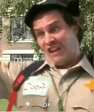 A Man Wearing A Hat And A Name Tag With The Word Ok On It GIF
