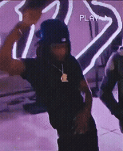 A Man Wearing A Hat And A Necklace Is Dancing In Front Of A Purple Background . GIF