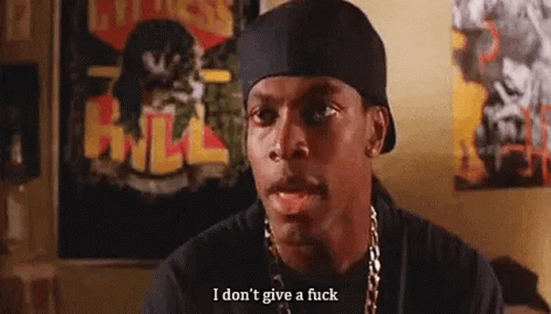 A Man Wearing A Hat And A Necklace Is Sitting In Front Of A Wall With Posters On It . GIF