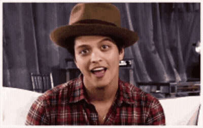 A Man Wearing A Hat And A Plaid Shirt Is Sitting On A Couch And Making A Funny Face . GIF