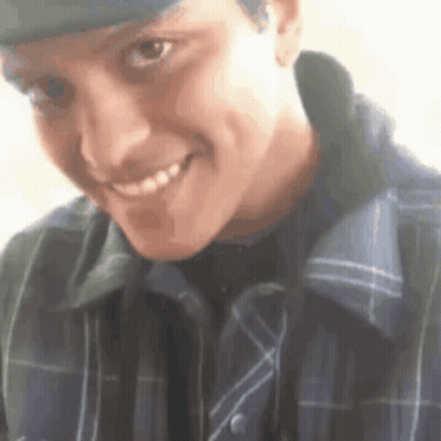A Man Wearing A Hat And A Plaid Shirt Is Smiling For The Camera . GIF