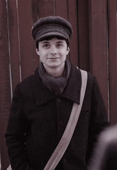 A Man Wearing A Hat And A Scarf Is Standing In Front Of A Wooden Fence GIF