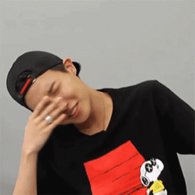 A Man Wearing A Hat And A Snoopy Shirt Covering His Face With His Hand . GIF