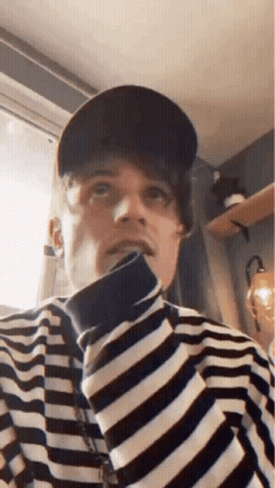 A Man Wearing A Hat And A Striped Shirt Is Looking Up At The Camera . GIF