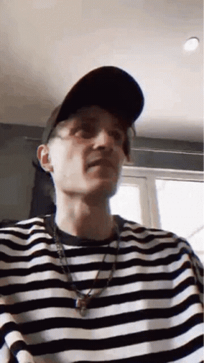 A Man Wearing A Hat And A Striped Shirt Is Making A Face . GIF