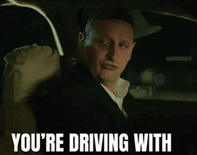 A Man Wearing A Hat And A Suit Is Driving A Car GIF