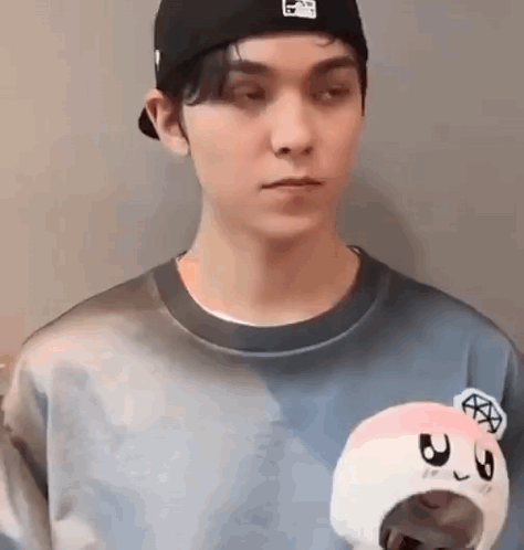 A Man Wearing A Hat And A Sweater Is Holding A Stuffed Animal . GIF