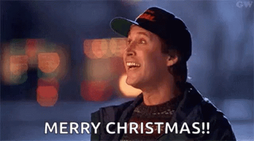 A Man Wearing A Hat And A Sweater Is Laughing And Saying Merry Christmas . GIF