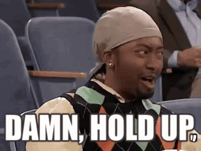A Man Wearing A Hat And A Sweater Is Sitting In A Stadium With The Words `` Damn , Hold Up '' . GIF
