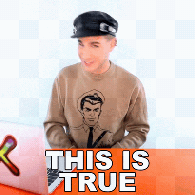 A Man Wearing A Hat And A Sweater That Says This Is True Sits In Front Of A Laptop GIF