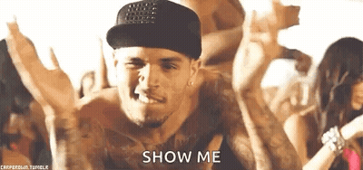 A Man Wearing A Hat And A Tank Top Is Dancing In Front Of A Crowd And Says `` Show Me '' . GIF