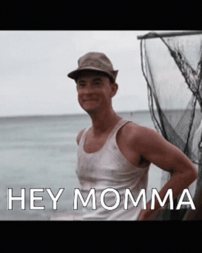 A Man Wearing A Hat And A Tank Top Is Standing In Front Of A Body Of Water And Says Hey Momma GIF