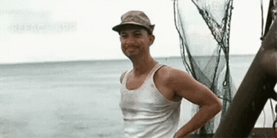 A Man Wearing A Hat And A Tank Top Is Standing On A Boat Near The Ocean . GIF