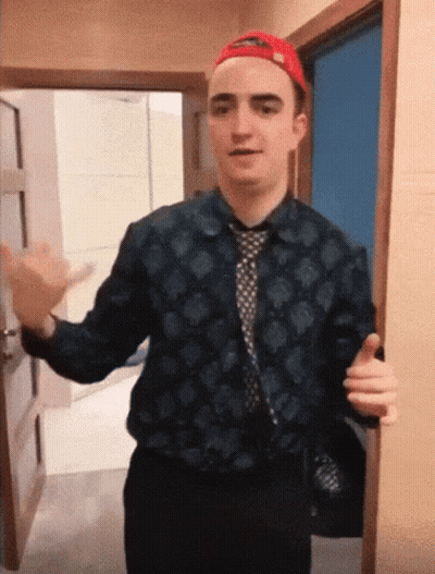 A Man Wearing A Hat And A Tie Is Standing In A Doorway GIF