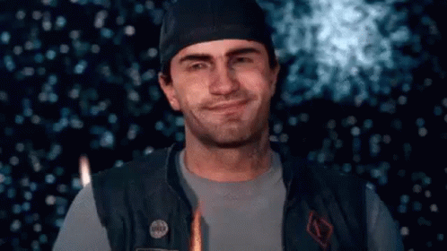 A Man Wearing A Hat And A Vest Is Smiling In Front Of A Firework Display . GIF