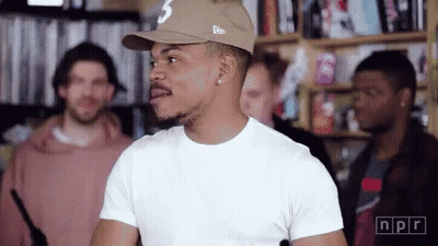 A Man Wearing A Hat And A White T-Shirt Is Standing In A Room With Other People . GIF
