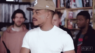 A Man Wearing A Hat And A White T-Shirt Is Standing In Front Of A Group Of Men . GIF