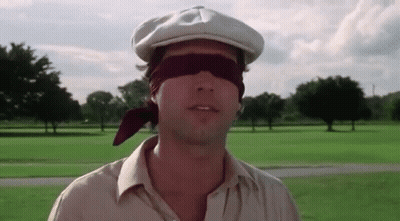 A Man Wearing A Hat And Blindfold Is Standing In A Field . GIF