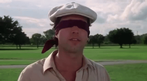 A Man Wearing A Hat And Blindfold Is Standing In A Field . GIF