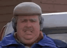A Man Wearing A Hat And Ear Muffs Is Making A Funny Face While Sitting In A Car . GIF