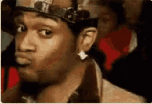 A Man Wearing A Hat And Earring Is Looking At The Camera . GIF