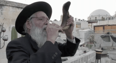 A Man Wearing A Hat And Glasses Is Blowing A Shofar Horn GIF