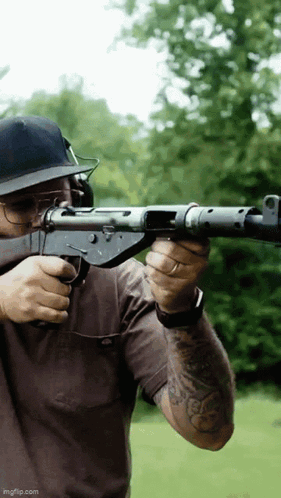 A Man Wearing A Hat And Glasses Is Holding A Gun GIF