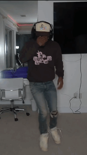 A Man Wearing A Hat And Headphones Is Standing In A Living Room GIF