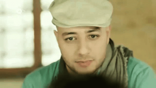 A Man Wearing A Hat And Scarf Looks At The Camera . GIF