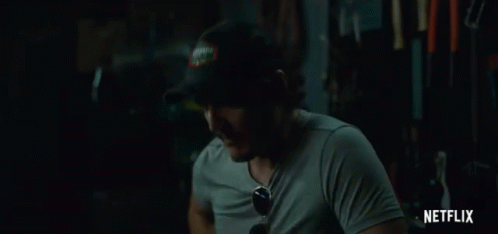 A Man Wearing A Hat And Sunglasses Is Sitting In A Dark Room With A Netflix Logo In The Corner . GIF