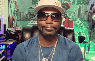 A Man Wearing A Hat And Sunglasses Is Sitting In Front Of A Sign That Says " On Air " GIF