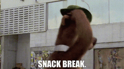 A Man Wearing A Hat And Sunglasses Is Standing In Front Of A Building With The Words `` Snack Break '' Written On It . GIF