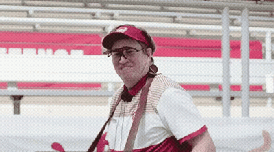 A Man Wearing A Hat And Sunglasses Is Standing In Front Of A Red And White Bench . GIF