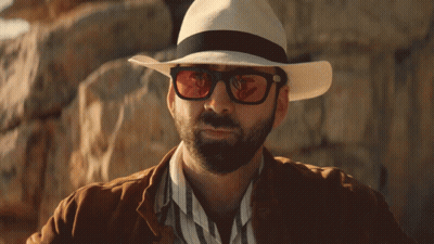 A Man Wearing A Hat And Sunglasses Is Standing In Front Of A Rock Wall GIF