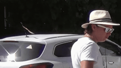 A Man Wearing A Hat And Sunglasses Is Standing In Front Of A White Suv . GIF