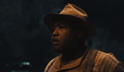 A Man Wearing A Hat And Suspenders Looks To His Left GIF