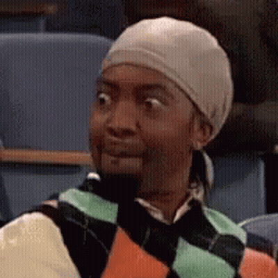 A Man Wearing A Hat And Sweater Is Sitting In A Classroom . GIF