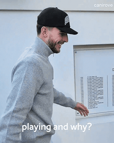 A Man Wearing A Hat And Sweater Is Standing In Front Of A Sign That Says " Playing And Why " GIF