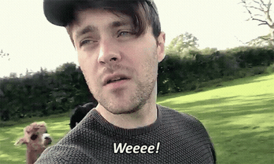 A Man Wearing A Hat And Sweater Says Weeeee While Standing In A Field GIF