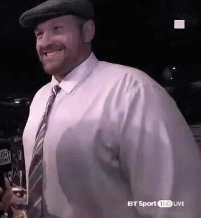 A Man Wearing A Hat And Tie Is Smiling And Holding A Glass Of Beer . GIF