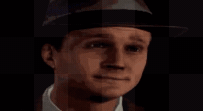 A Man Wearing A Hat And Tie Is Standing In Front Of A Blue X . GIF