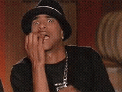 A Man Wearing A Hat Is Biting His Nails And Making A Funny Face . GIF