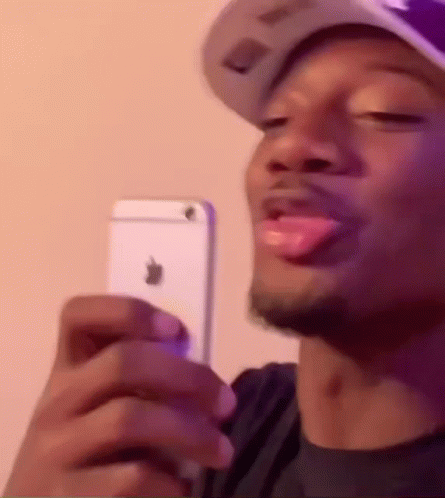 A Man Wearing A Hat Is Holding A White Iphone In His Hand . GIF