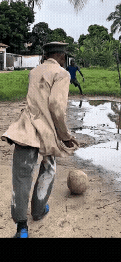A Man Wearing A Hat Is Kicking A Soccer Ball In A Muddy Field . GIF