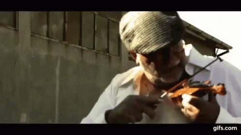 A Man Wearing A Hat Is Playing A Violin In Front Of A Building .. GIF