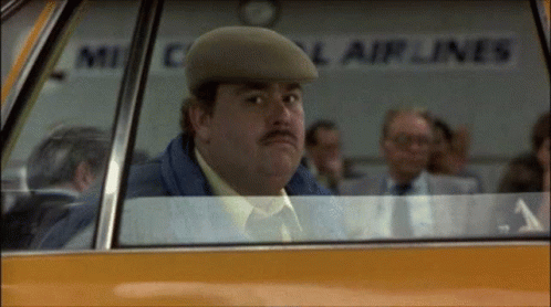 A Man Wearing A Hat Is Sitting In A Car With A Sign That Says Airlines In The Background GIF